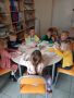 Siedmioro przedszkolaków z grupy „Słoneczka” siedzących przy stolikach i wykonujących zadania plastyczne.