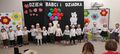 Dzieci z grupy Gwiazdeczek stoją na tle dekoracji z okazji Dnia Babci i Dziadka