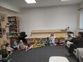 Dzieci siedzace na dywanie z nauczycilem Pani Alinka pokazuje ksiazke