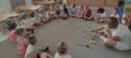 Nauczyciel turla piłeczkę siedzacym dzieciom w kole na dywanie