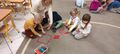 Czworka dzieci z nauczycielem ukladaja z kolorowych patyczkow na dywanie