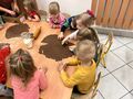Dzieci z grupy Gwiazdeczek siedzą przy stole i wykrawają gotowymi formami ciastka