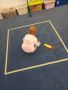 Dziewczynka uklada kwadratowe klocki w duzym kwadracie przyklejonym na dywanie