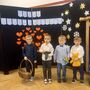 Czterech chłopców stoi na tle dekoracji do przedstawienia z okazji dnia babci i dziadka i tzrymaja kosz auto buty i misia