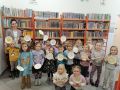 Bibliotekarka i dzieci z grupy Sloneczka stoja na tle ksiazek w szkolnej bibliotecejpg