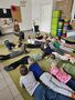 Dzieci z grupy Promyczki leżą na dywanie i słuchają bajki czytanej przez Panią Patrycję